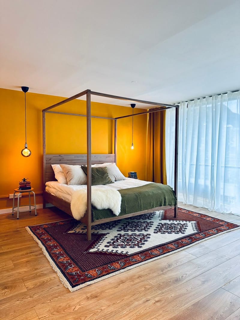 Himmelbett vor senfgelber Wand mit Orientteppich in den Emmas Lofts